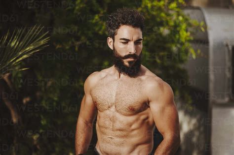 Attractive Shirtless Man Standing In Front Of Shrubs Stock Photo