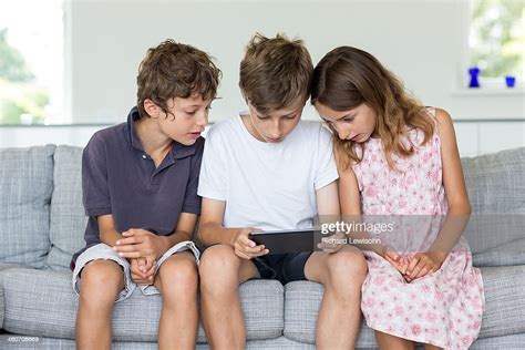 Brothers And Sister On Sofa Looking At Digital Tablet High Res Stock