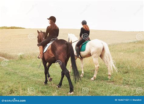 Two Young Pretty Girls Riding A Horses On A Field They Loves Animals
