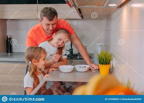 a father feeds his daughters in the kitchen on a background of fruits stock image image of