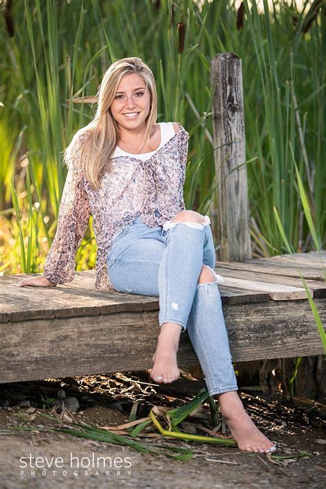 Blonde Teen In Jeans And Patterned Blouse Sits Cross Legged On Dock