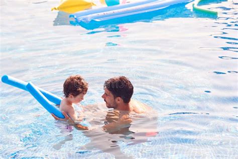 Father And Son In Outdoor Pool On Summer Vacation Teaching Son To Swim