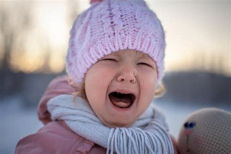 Portrait Of A Sad Crying Blonde Little Girl In A Pink Knitted Hat And A