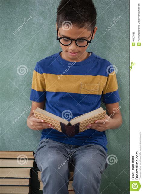 Schoolboy Sitting On Books Stack And Reading Book Stock Photo Image