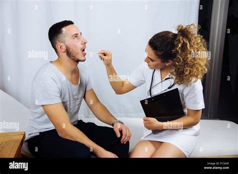 Young Female Doctor Checking Throat Of A Male Patient In Private