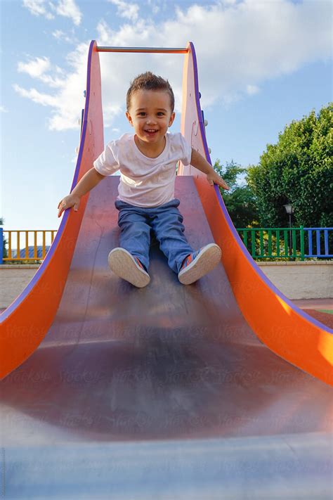 Child Sliding Down A Slide In A Playground Del Colaborador De Stocksy