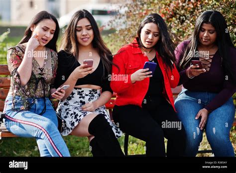 group of four happy and pretty latino girls from ecuador posed at street and looking at mobile