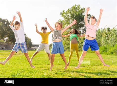 Happy School Children Jumping On The Green Lawn In Park Stock Photo Alamy