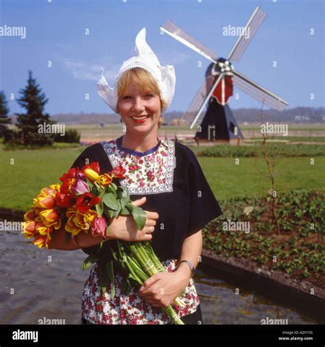 Dutch Girl In Traditional Costume Holding A Huge Bunch Of Red And Yellow Tulips With Windmill In