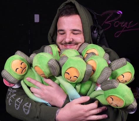 A Man In A Hoodie Holding A Bunch Of Stuffed Animals With Faces On Them