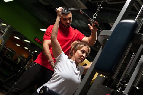 Young Male Coach Assisting Female Client In Gym Stock Photo Download