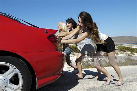 Three Young Women Pushing Red Car Along Road High Res Stock Photo