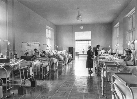 Black And White Photograph Of People In A Hospital Room With Cots On