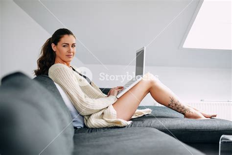Portrait Of Young Woman On A Couch With A Laptop Looking At Camera Female Model Indoors On