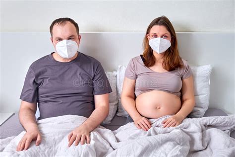 A Man And A Pregnant Woman In A Face Mask Are Sitting In Bed Husband