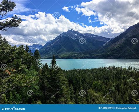 A View Of A Majestic Turquoise Lake Surrounded By Vast Green Evergreen