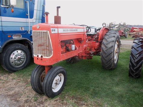 An Old Red Tractor Parked Next To A Blue And White Truck On The Grass