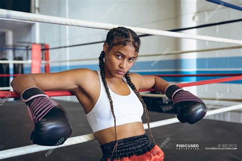 Female Boxer With Boxing Gloves Leaning On Ropes And Looking At Camera