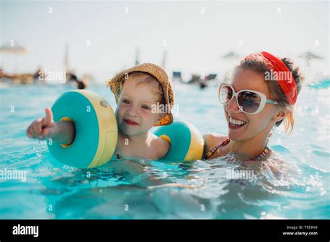 A Small Toddler Boy With Armbands And Mother Swimming In Water On