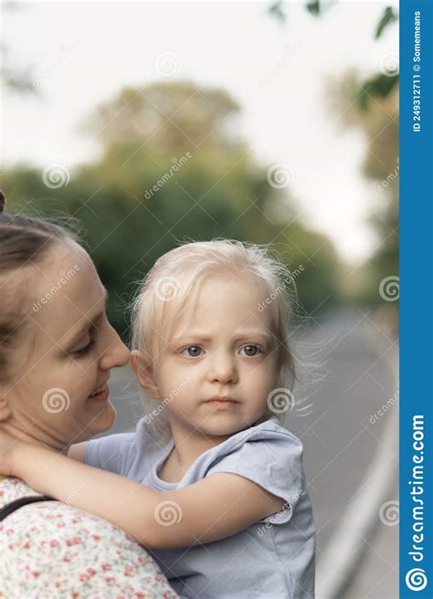 Young Mother Holds Serious Daughter In Her Arms And Smiling Sweetly