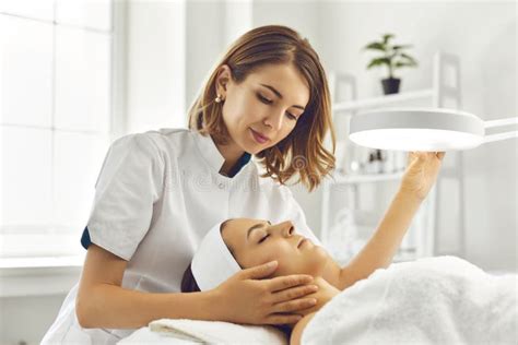 Cosmetologist Directing Lamp To Woman For Facial Treatment Stock Image