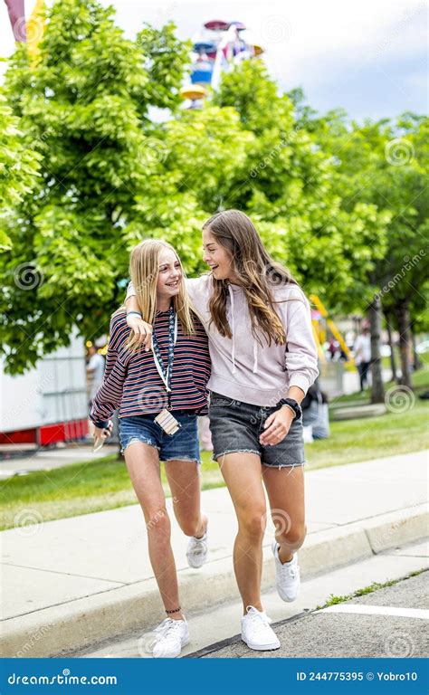 Two Smiling Teenage Girls Walking Together At An Outdoor Carnival