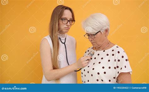 Young Woman Doctor Or Nurse Using Stethoscope On Senior Woman Stock
