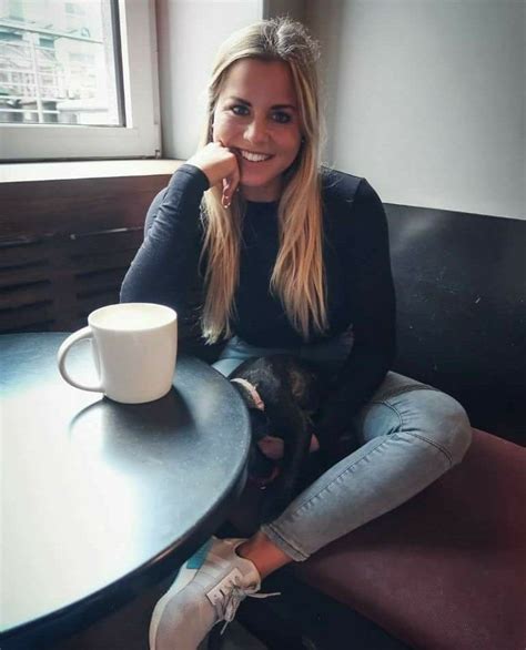 A Woman Sitting At A Table With A Coffee Cup In Front Of Her And A Black Cat On Her Lap