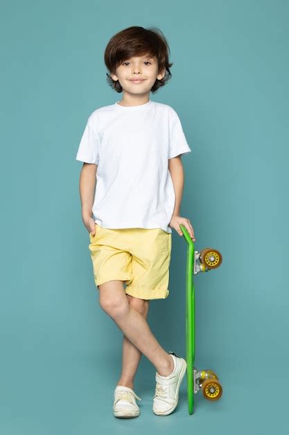 widok z przodu ładny chłopiec dziecko w białej koszulce i żółtych dżinsach z zieloną deskorolką