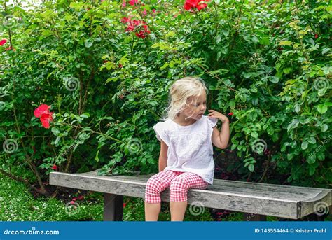 Little Blonde Girl Sitting On A Bench In The Garden Stock Photo Image