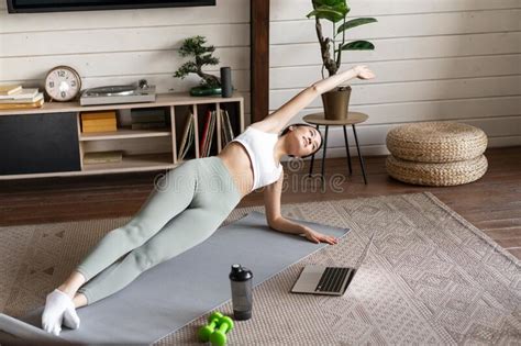 Young Asian Woman Doing Workout At Home On Floor Mat Following Sport Instructor On Laptop Video