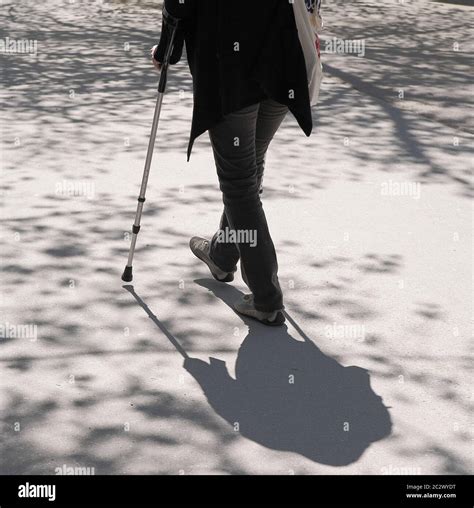 One Person With Crutch Walking On Concrete With Tree Shadows