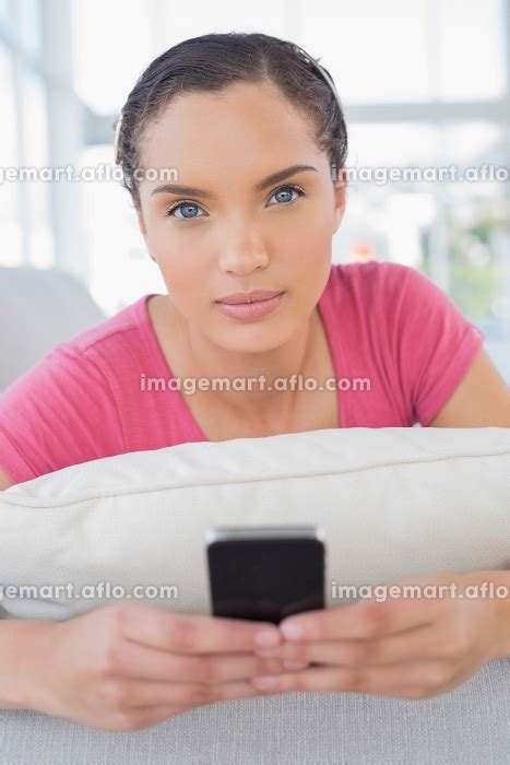 Serious woman lying on sofa and texting while looking at cameraの写真素材 イメージマート