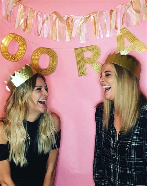 Two Women Standing Next To Each Other In Front Of A Pink Wall With Gold