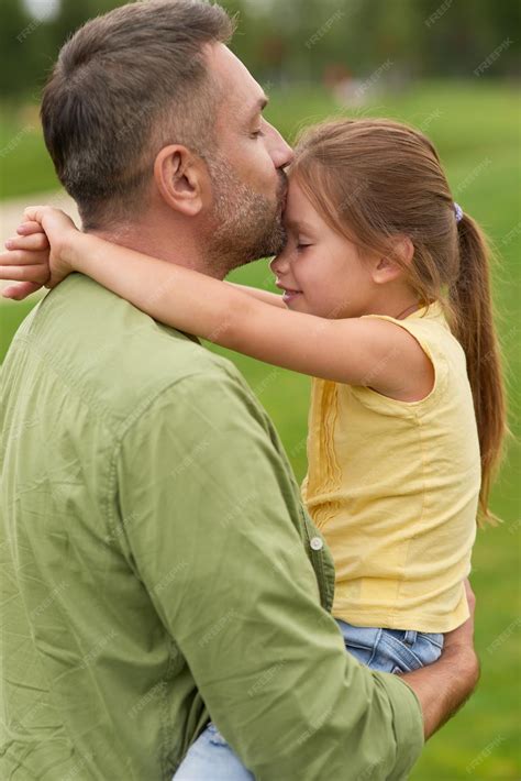 야외에서 함께 시간을 보내는 동안 어린 소녀를 안고 키스하는 감사하는 아빠의 측면 프리미엄 사진