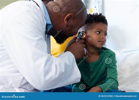 African American Male Doctor Using Otoscope To Examine Ear Of Boy