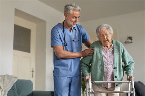 Caregiver Helping Senior Woman To Walk With Walker In Her Home Stock