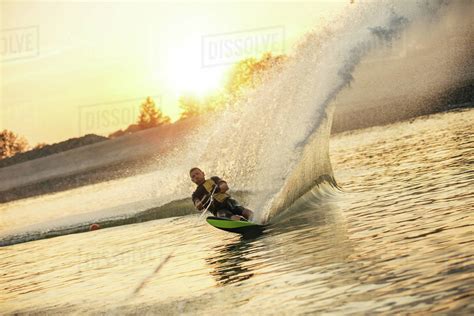 Waterskier Moving Fast In Splashes Of Water At Sunset Man Wakeboarding