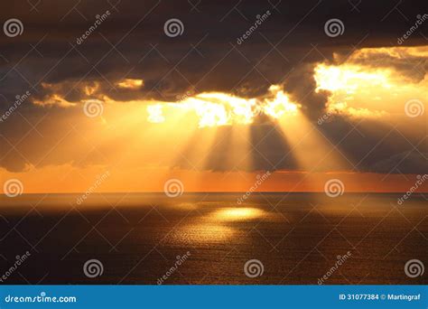 Sunbeams Through Dark Clouds Over Ocean By Golden Sunrise Stock Photo