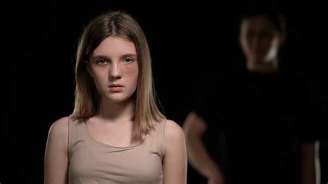 frightened beaten teenage girl looking with fear back at blurred woman holding belt portrait of