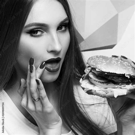 portrait of playful beautiful sexy woman with red lips holding delicious hamburger and looking