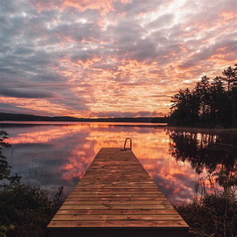 A Wooden Dock Sitting On Top Of A Lake Under A Colorful Sky With Clouds