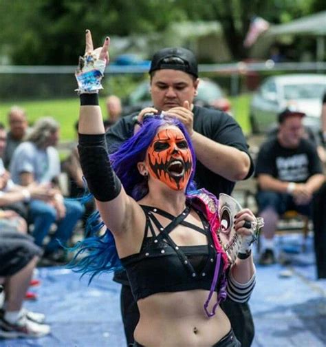 A Woman With Purple Hair And Painted Face Is Being Held Up By A Man In Black