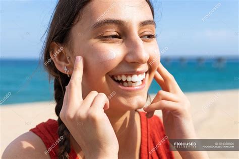 Smiling Female Applying Suntan Lotion On Face On Sunny Day In Summer In