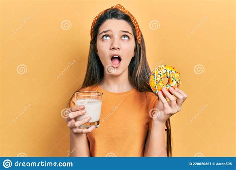 Young Brunette Girl Eating Donut And Drinking Glass Of Milk Angry And