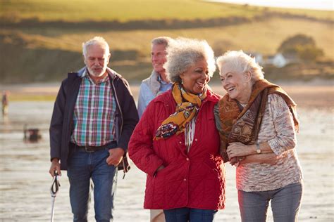 Group Of Smiling Senior Friends Walking Arm In Arm Along Shoreline Of 
