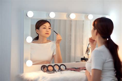 Reflection Of Young Beautiful Woman Applying Her Make Up Looking In A