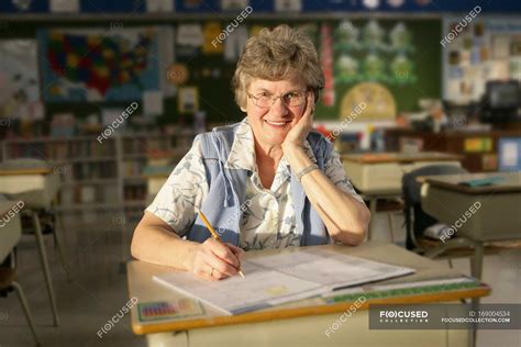 Happy Mature Female Teacher Sitting At School Desk — Caucasian