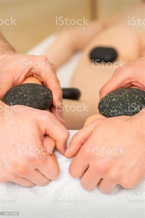 Two Masseurs Make A Foot Massage With A Hot Stone In Four Hands At The