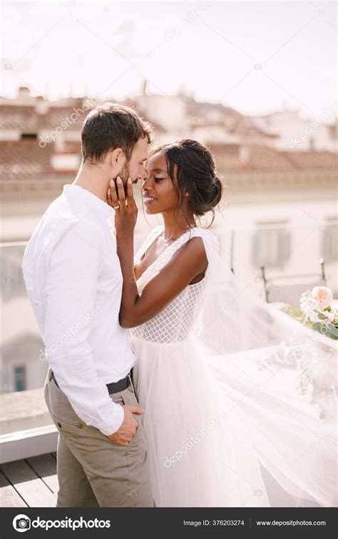 mixed race wedding couple caucasian groom and african american bride cuddling on a rooftop in